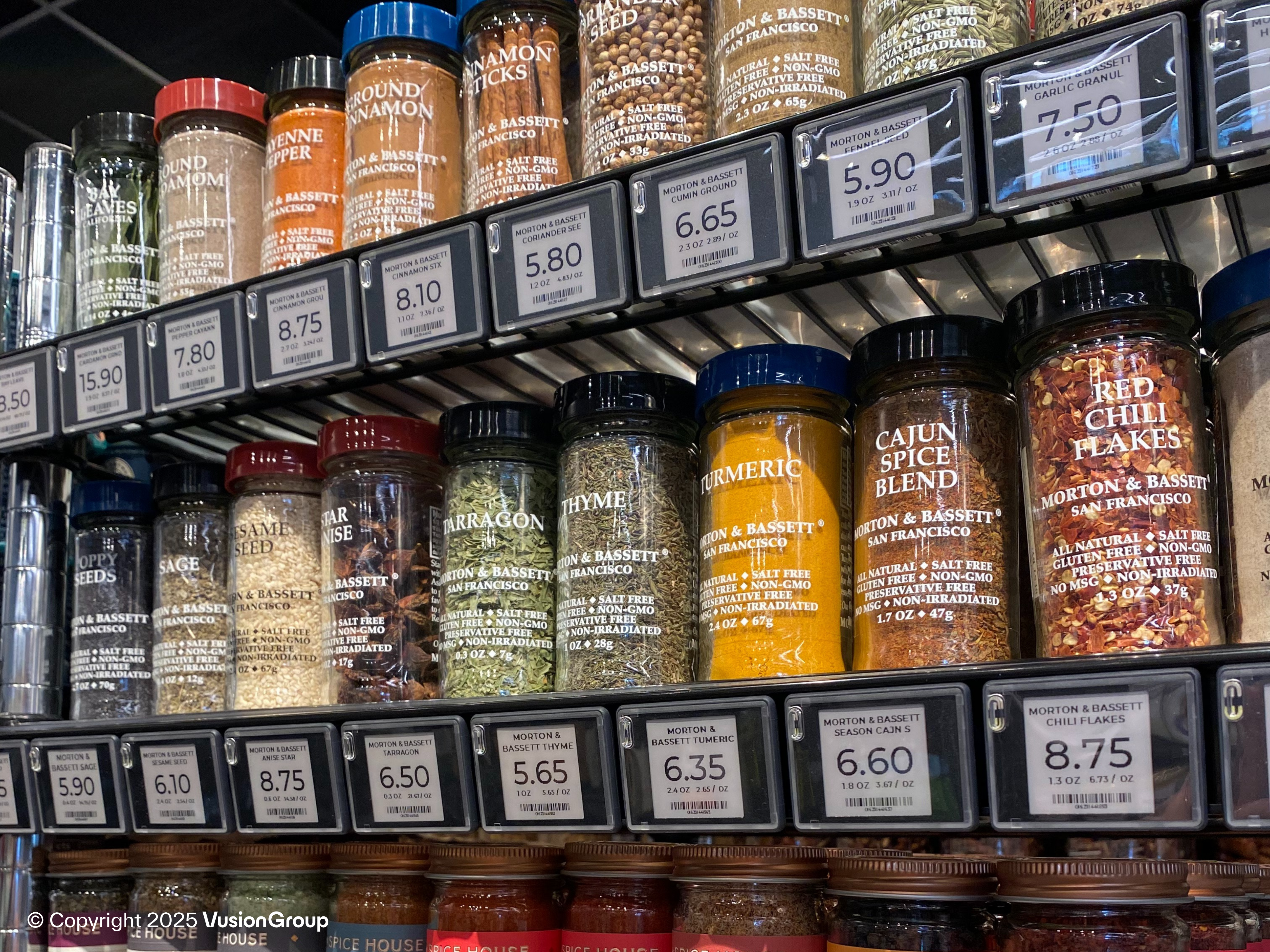 Spice aisle with jars and precise digital price tags across the shelf edge, using DUMAC electronic shelf labels (SES-imagotag Vusion).